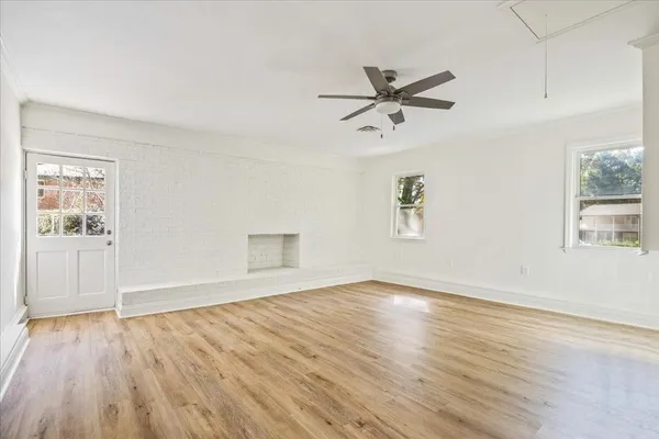 an empty room with wooden floor a ceiling fan and windows