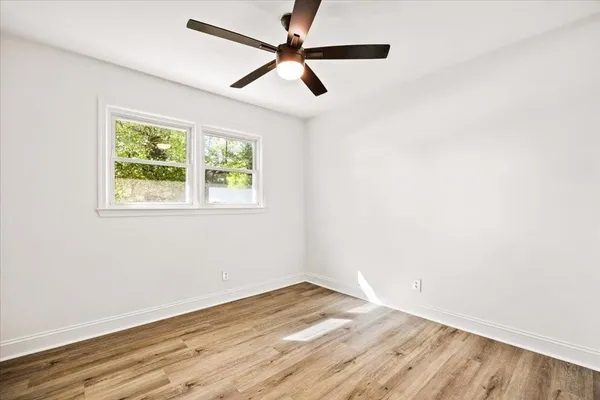 an empty room with wooden floor ceiling fan and windows