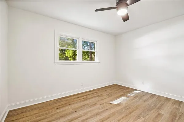 an empty room with wooden floor fan and windows