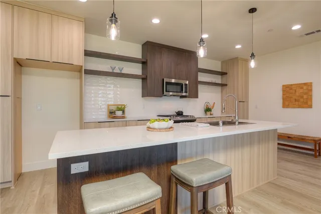 a large kitchen with stainless steel appliances kitchen island granite countertop a large counter top a sink dishwasher a stove and a dining table with wooden floor