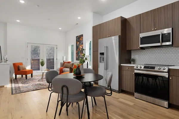 a kitchen with stainless steel appliances a stove a refrigerator a microwave a dining table and chairs with wooden floor