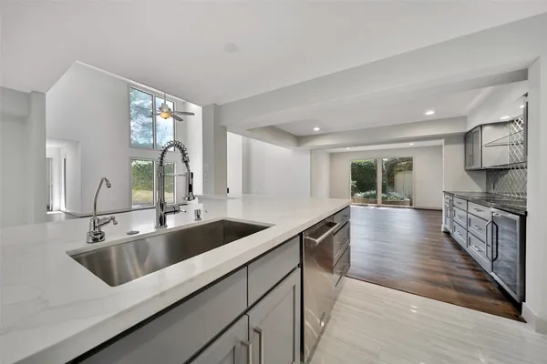 a view of a kitchen counter top space with stainless steel appliances a sink wooden floor and a large window