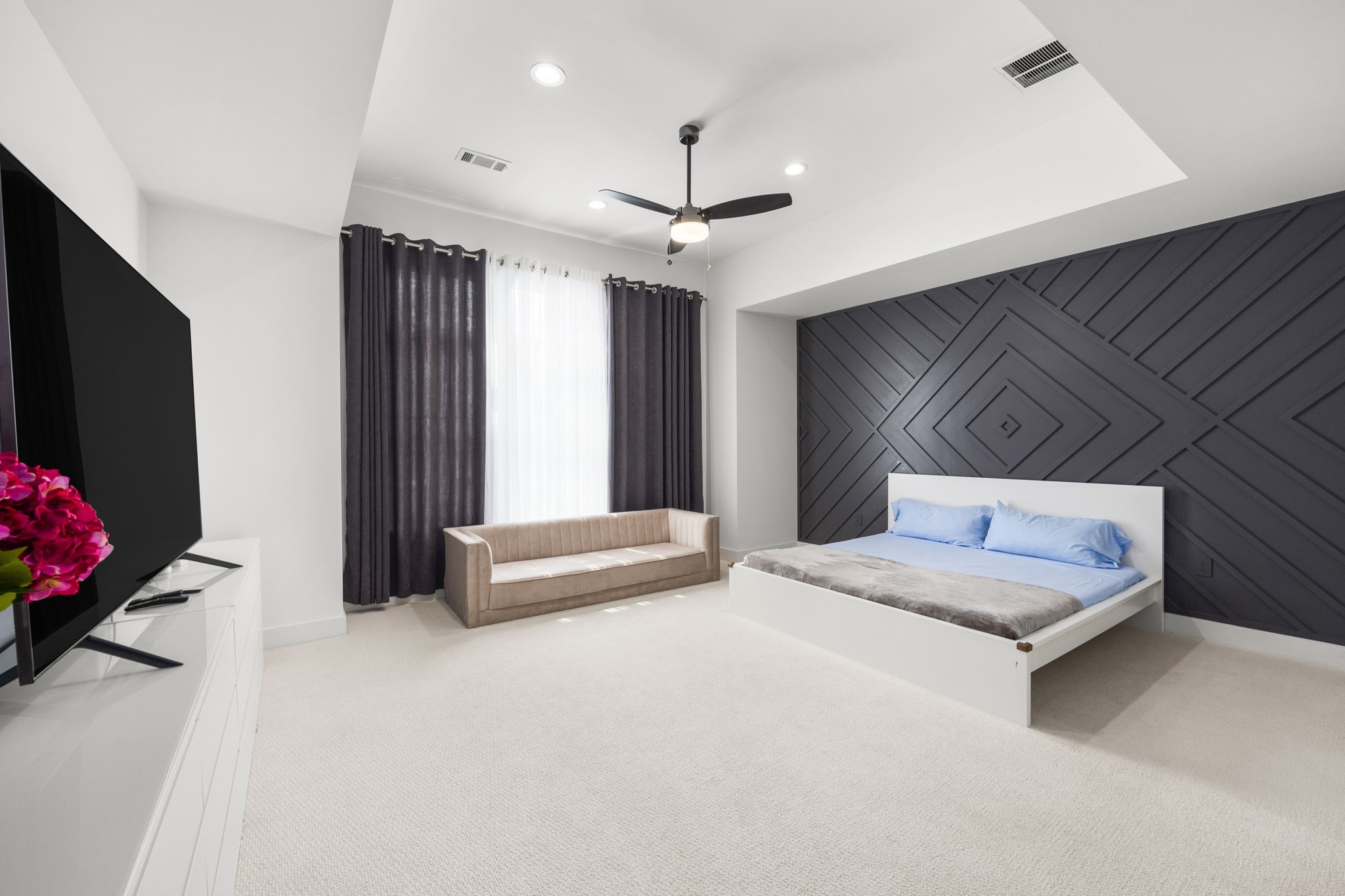 2411 Hazard Street Houston, TX 77019 - Photo 4 of 46 This view of the primary bedroom highlights a striking wood-paneled accent wall that adds texture and depth to the space. The recessed ceiling with modern lighting complements the clean, minimalist design, creating a sophisticated and tranquil retreat.