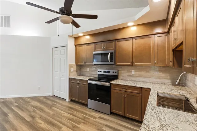 a kitchen with stainless steel appliances granite countertop a sink and a stove top oven with wooden floor