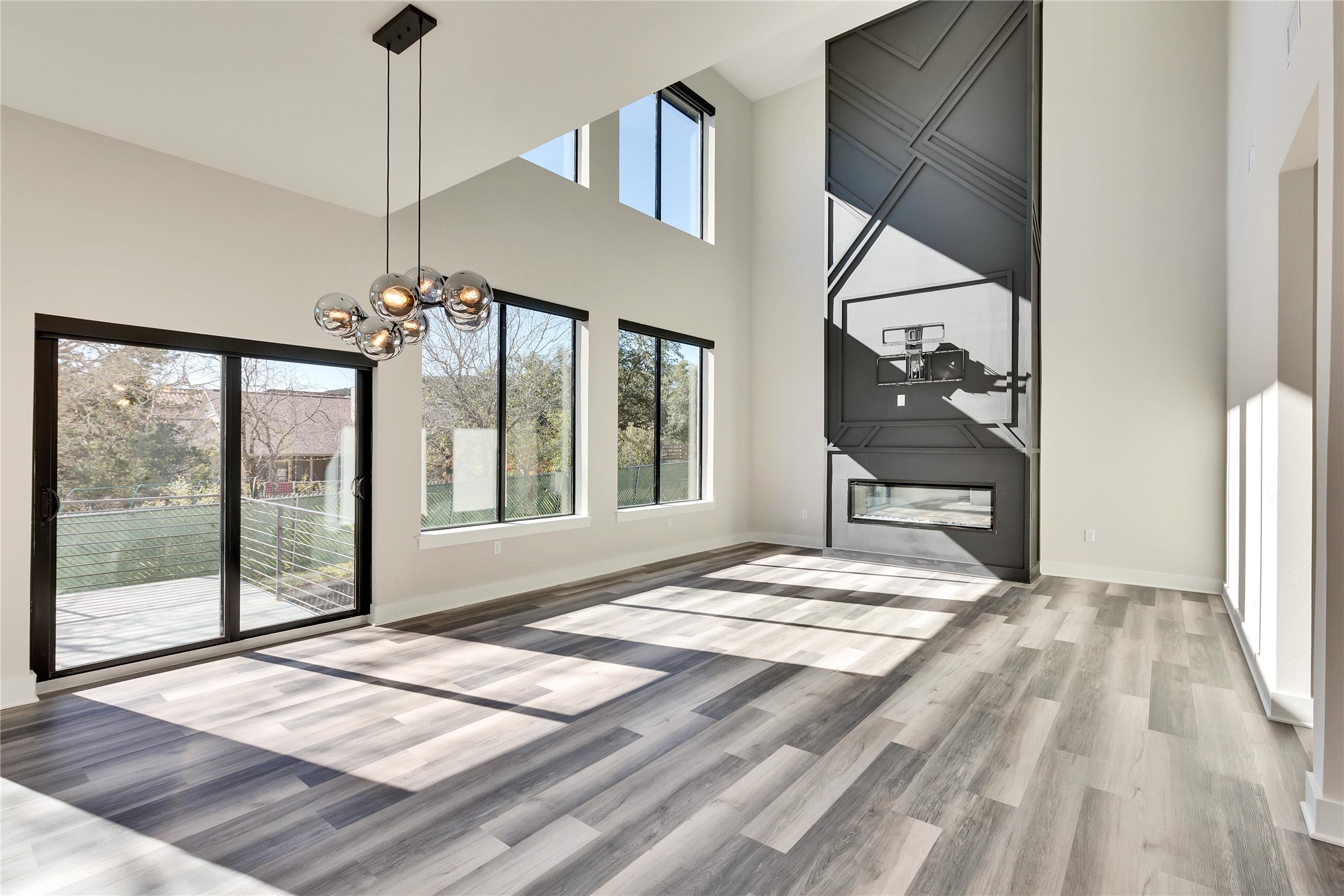 1304 Minnie Drive Austin, TX 78732 - Photo 9 of 28 Unfurnished living room with a high ceiling, suspended lighting, light wood-style flooring, and a large fireplace