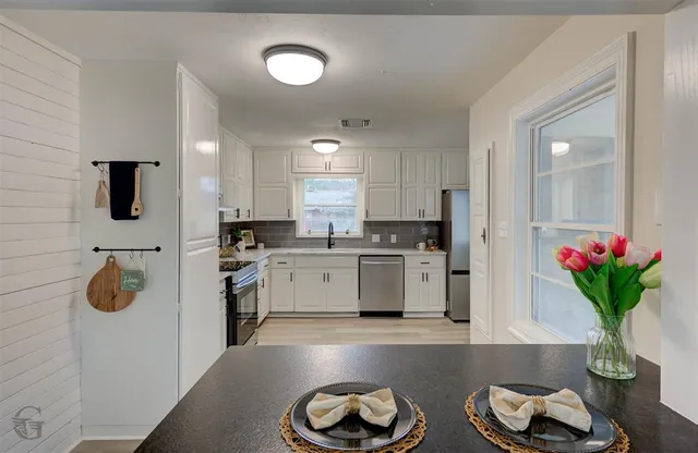 a kitchen with stainless steel appliances kitchen island granite countertop a refrigerator a stove a sink dishwasher and white cabinets with wooden floor