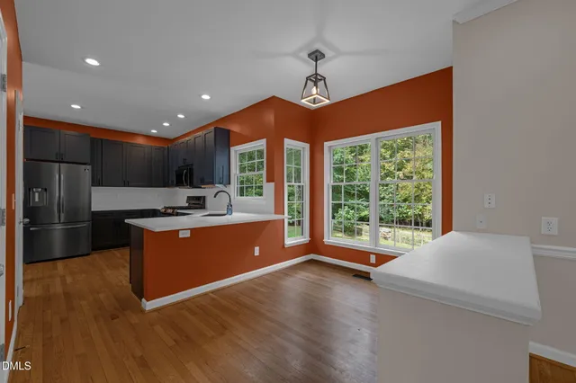 a open kitchen with stainless steel appliances granite countertop a refrigerator a sink dishwasher a stove and a large window with wooden floor