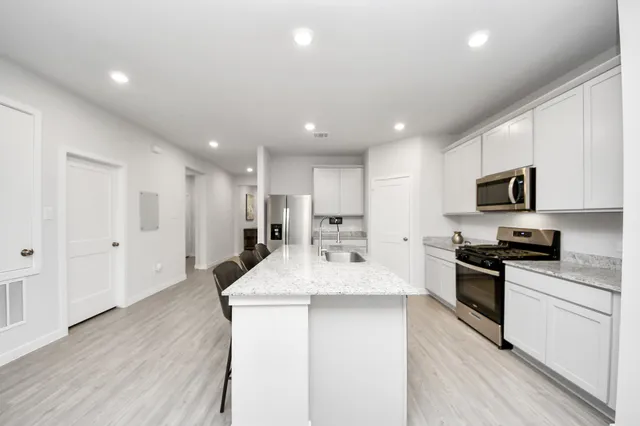 a kitchen with stainless steel appliances kitchen island granite countertop a sink and a stove top oven with wooden floor