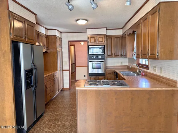 a kitchen with stainless steel appliances granite countertop a refrigerator a stove and a sink with wooden cabinets