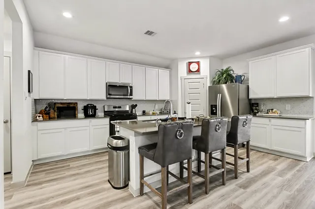 a kitchen with stainless steel appliances granite countertop a stove top oven a sink dishwasher a dining table and chairs with wooden floor