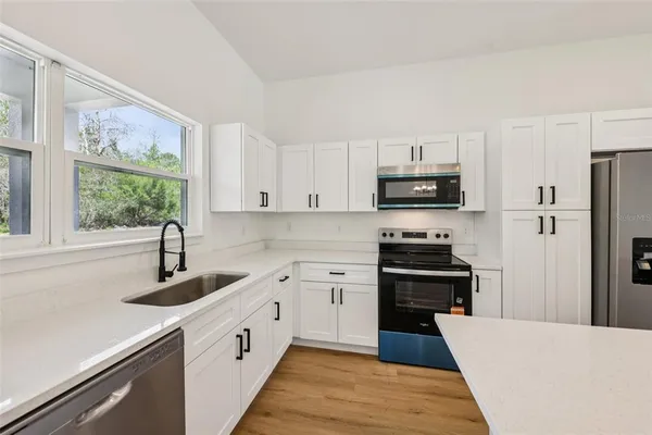 a kitchen with stainless steel appliances granite countertop a refrigerator a sink dishwasher a stove and a dining table with wooden floor