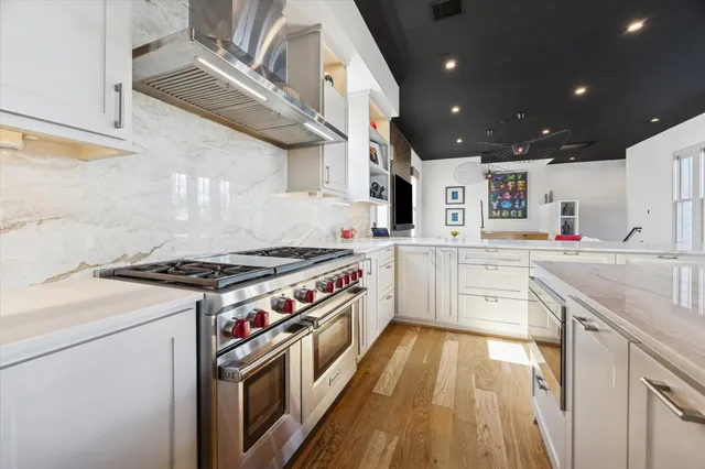 a kitchen with stainless steel appliances kitchen island granite countertop a stove a sink dishwasher and white cabinets with wooden floor