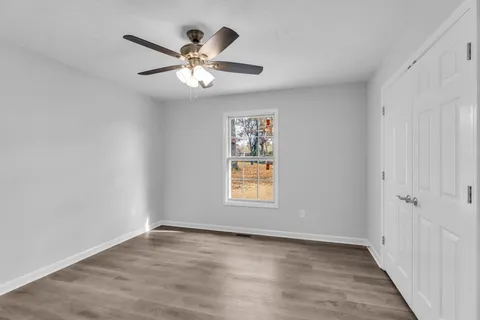 an empty room with wooden floor chandelier fan and windows
