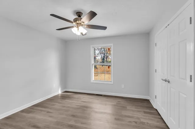 an empty room with wooden floor chandelier fan and windows