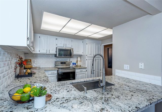 a kitchen with stainless steel appliances granite countertop a sink a stove a refrigerator cabinets a dining table and chairs