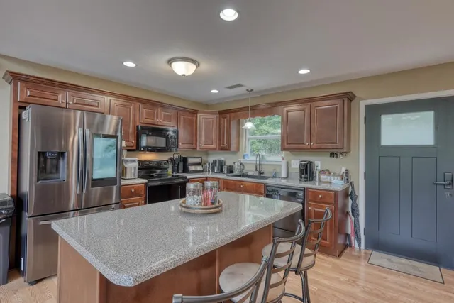 a kitchen with stainless steel appliances granite countertop a stove top oven a sink dishwasher a dining table and chairs with wooden floor