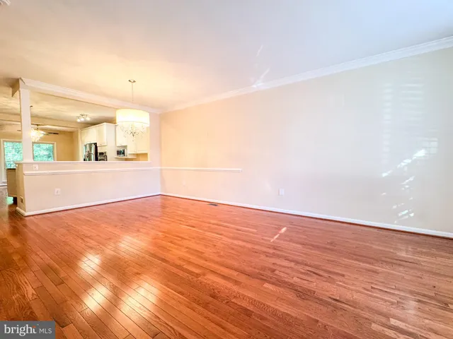 an empty room with wooden floor and kitchen view