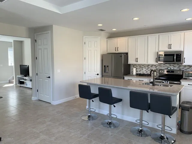 a kitchen with stainless steel appliances kitchen island granite countertop a stove top oven a refrigerator a sink and a dining table with white cabinets