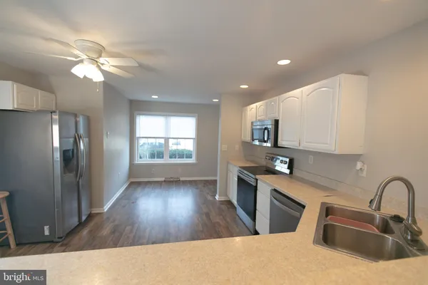 a kitchen with stainless steel appliances granite countertop a refrigerator a sink dishwasher a stove and white countertops with wooden floor