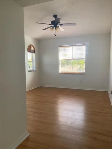 an empty room with wooden floor chandelier fan and windows