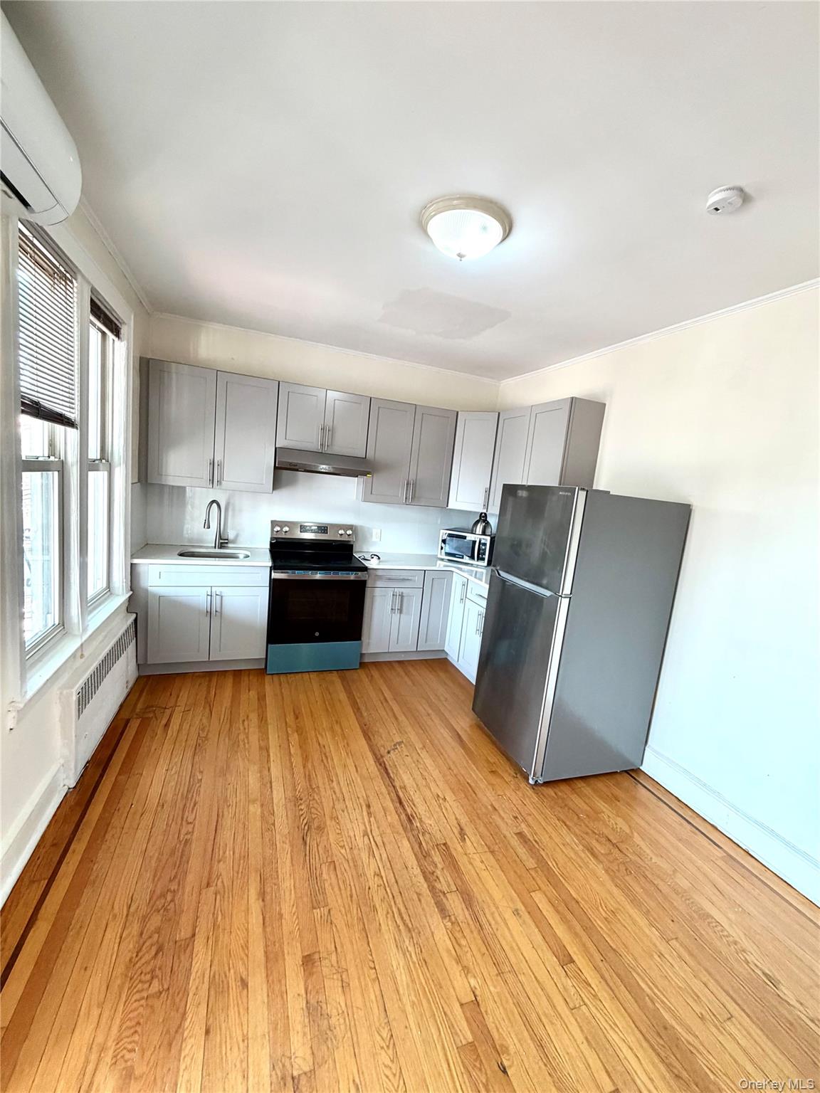 30-06 85th Street, Unit 2 Queens, NY 11370 - Photo 2 of 7 Kitchen with gray cabinetry, appliances with stainless steel finishes, light countertops, light wood-style flooring, and radiator