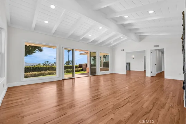an empty room with wooden floor chandelier and windows
