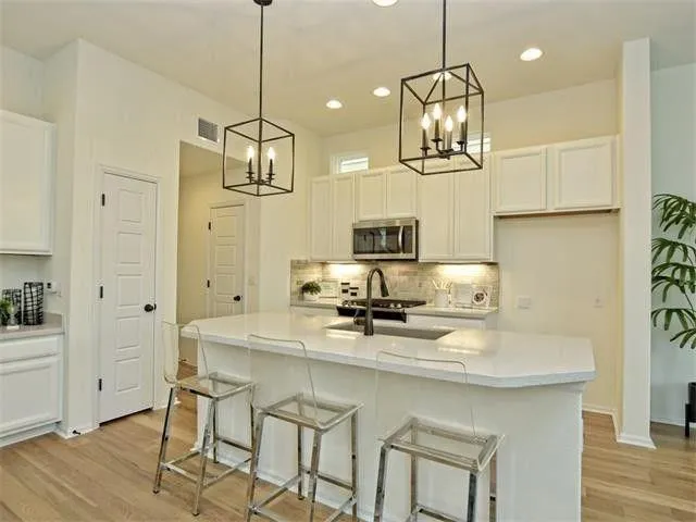 a kitchen with stainless steel appliances granite countertop a sink a refrigerator a stove a dining table and chairs with wooden floor