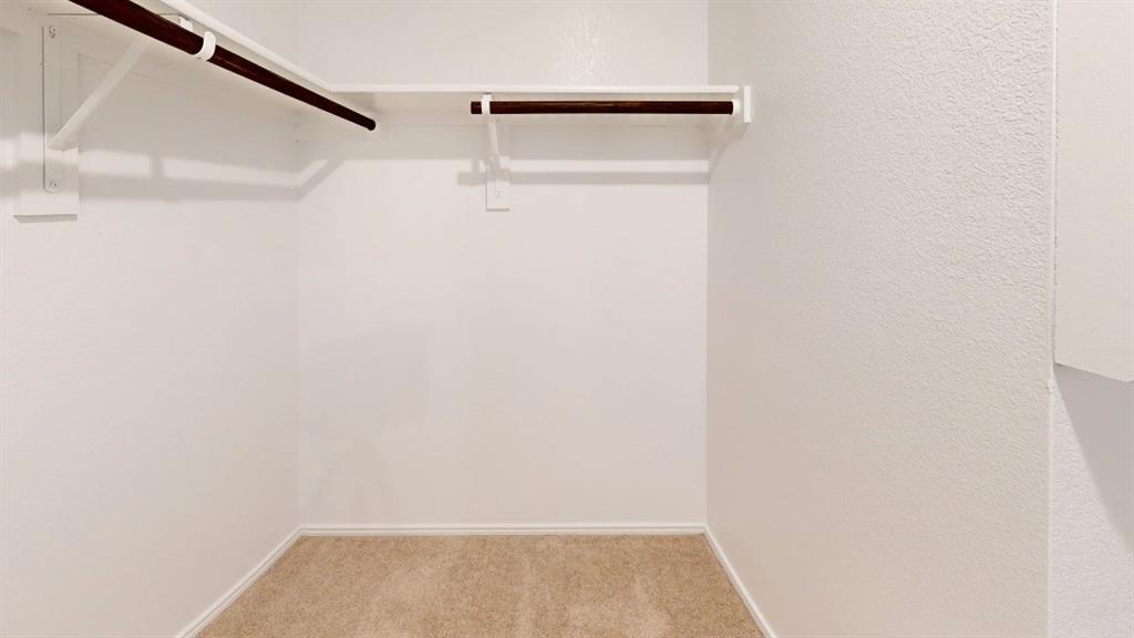 9757 Platteview Road Fort Worth, TX 76179 - Photo 16 of 19 Walk-in closet featuring light-toned carpeting, white textured walls, and integrated shelving with dark-toned hanging rods
