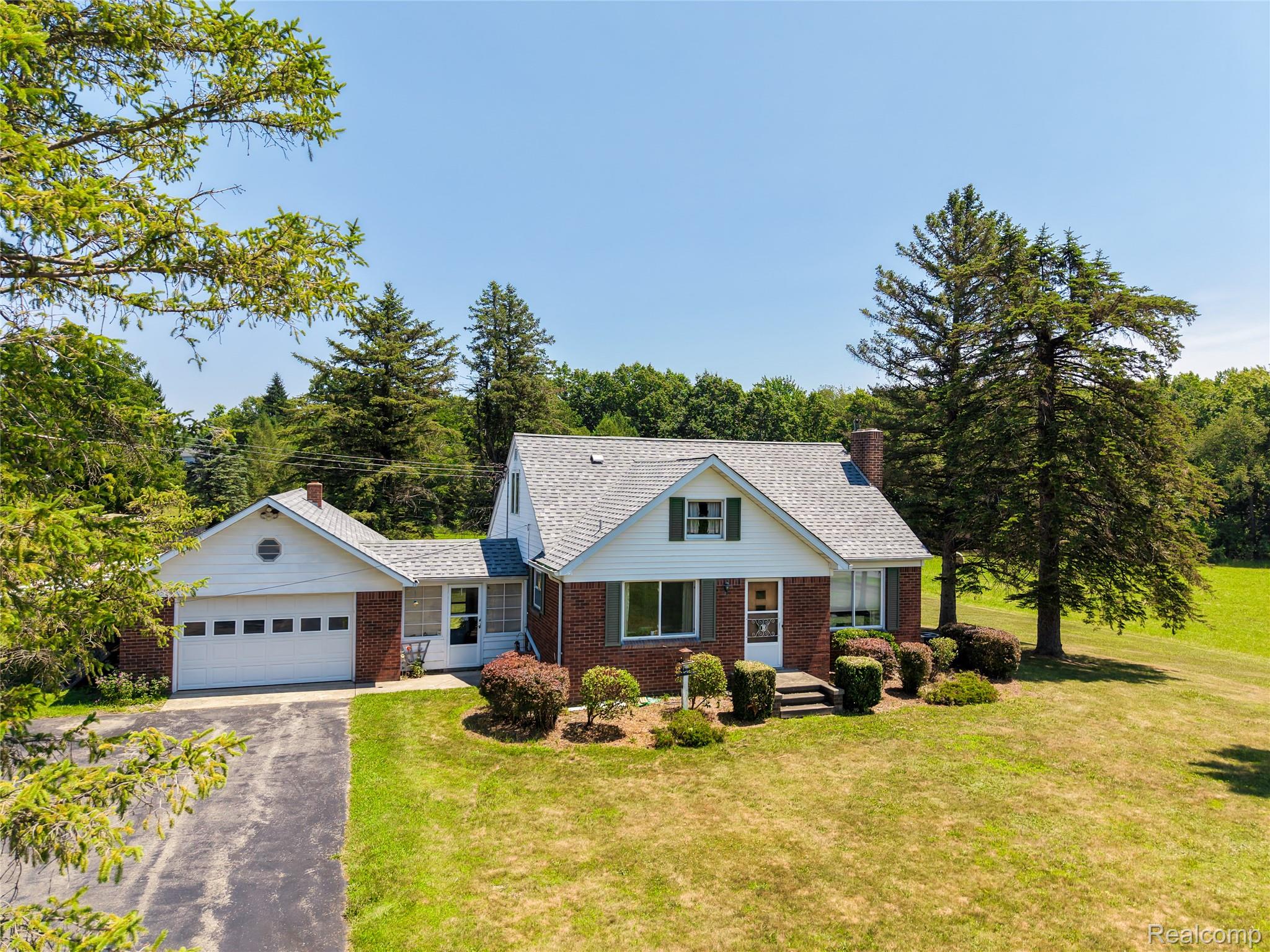 11651 South New Lothrop Road Byron, MI 48418 - Photo 1 of 19 Traditional-style residence featuring a brick and white siding facade, a two-car garage with an asphalt driveway, mature evergreen trees, and established front landscaping