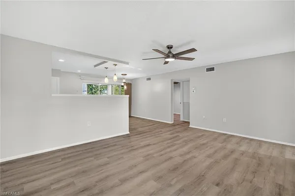 a view of an empty room with wooden floor and a ceiling fan