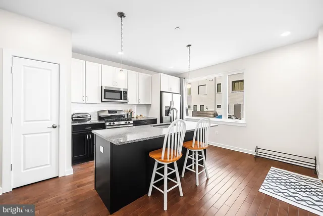 a kitchen with stainless steel appliances granite countertop a stove top oven a refrigerator a dining table and chairs with wooden floor