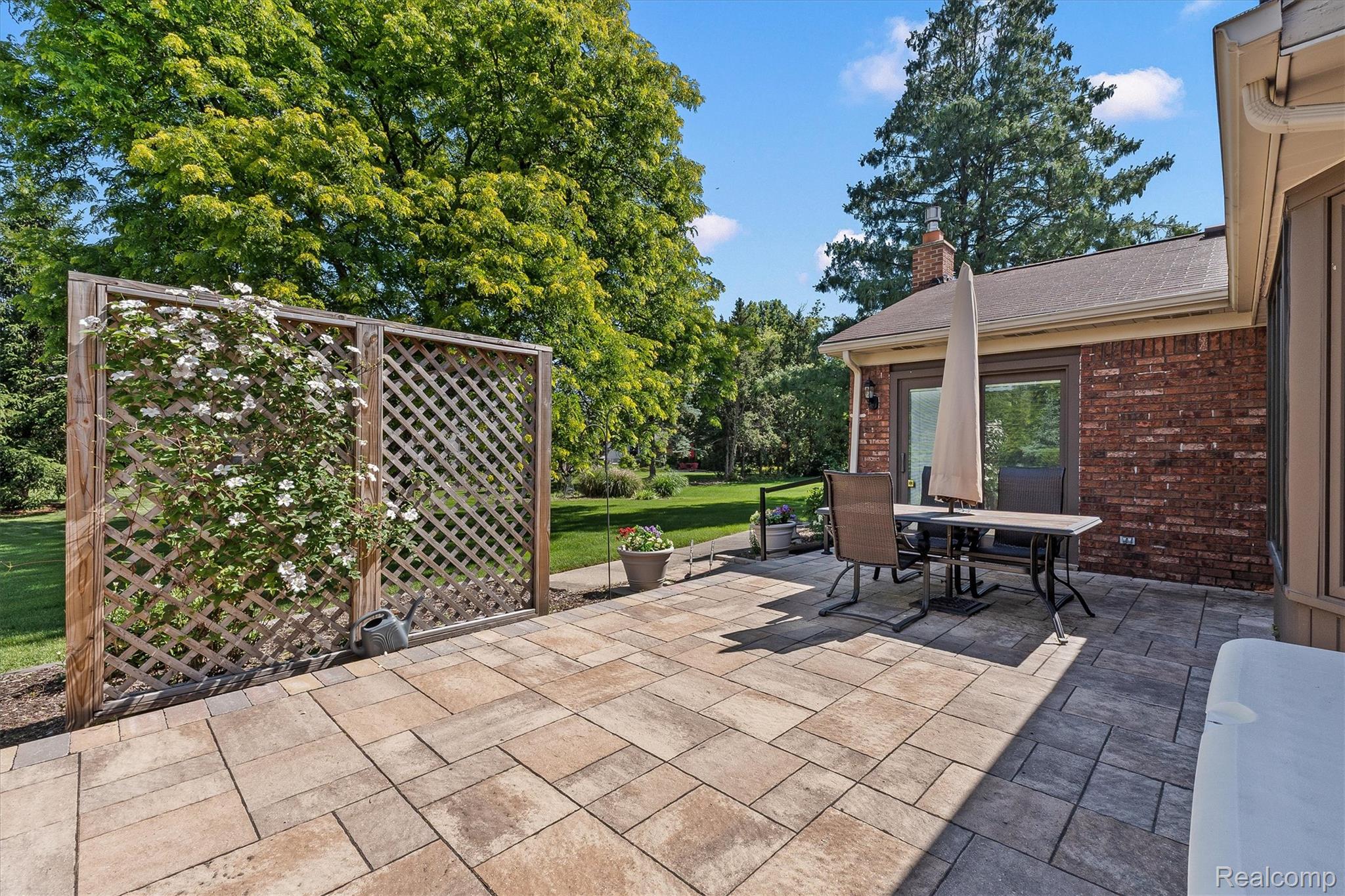 1662 Sumac Drive Rochester, MI 48309 - Photo 35 of 38 Expansive paver patio with a brick exterior, lattice privacy screen, and lush green landscaping