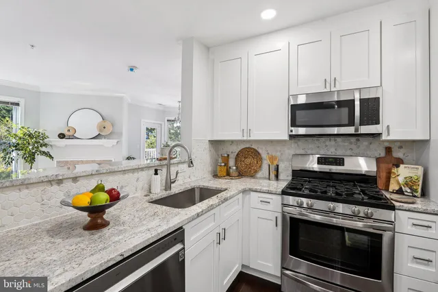 a kitchen with stainless steel appliances granite countertop a sink a stove a microwave cabinets and a wooden floor