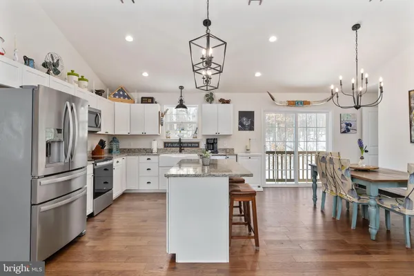 a kitchen with stainless steel appliances kitchen island granite countertop a dining table chairs and white cabinets