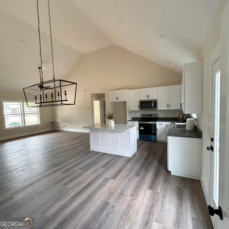 a kitchen with stainless steel appliances granite countertop a stove a sink dishwasher a refrigerator white cabinets and wooden floor