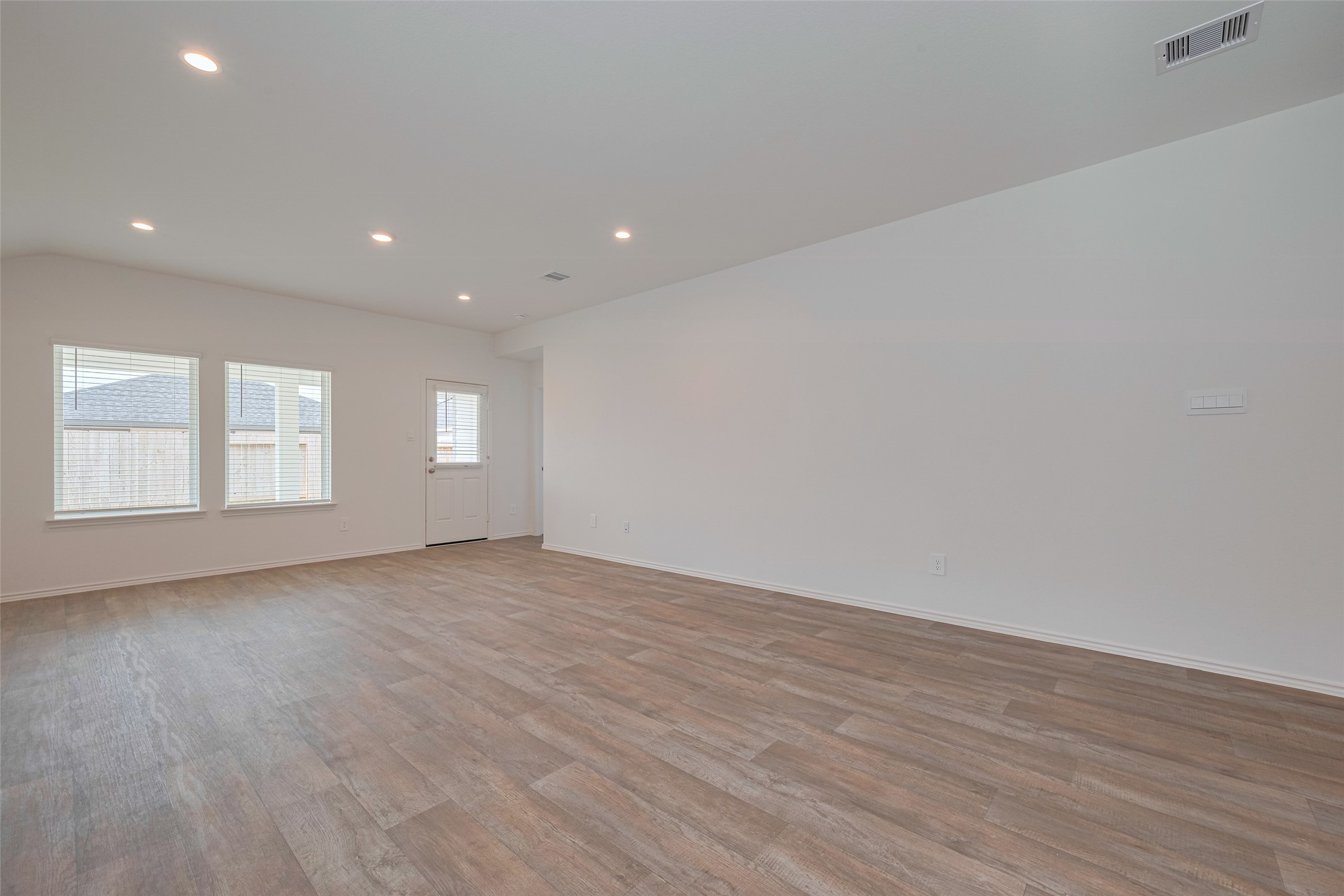 30842 Brightwell Bend Fulshear, TX 77441 - Photo 7 of 31 The spacious living room is filled with light from large windows and a glass paneled door that opens to the backyard. Recessed lighting highlights the rich wood-look flooring, creating an inviting space for relaxation and entertaining.