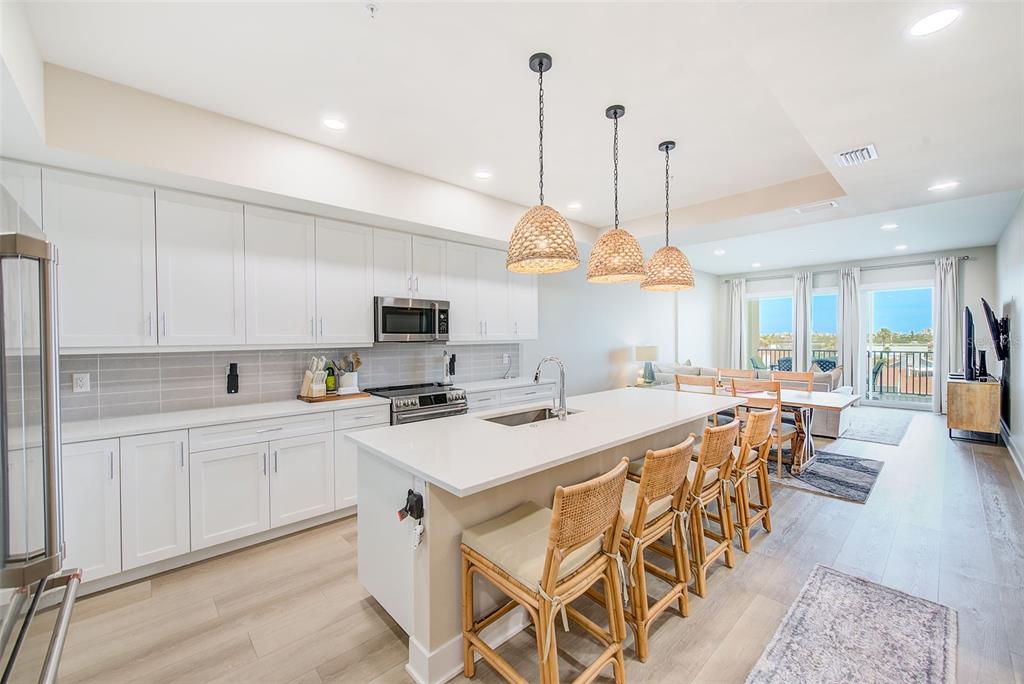 400 150th Avenue, Unit 504 Madeira Beach, FL 33708 - Photo 11 of 60 a kitchen with stainless steel appliances kitchen island granite countertop a stove a sink a dining table and chairs with wooden floor