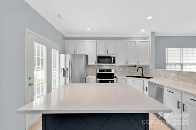 a kitchen with stainless steel appliances a stove a sink a microwave a refrigerator and white cabinets