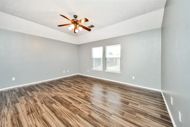 an empty room with wooden floor fan and windows