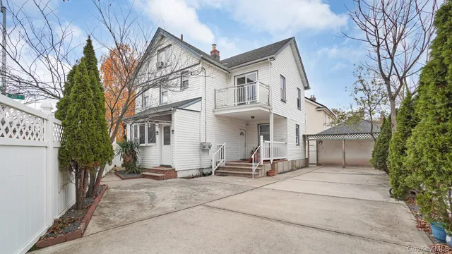 a view of a white house with a large tree and wooden fence