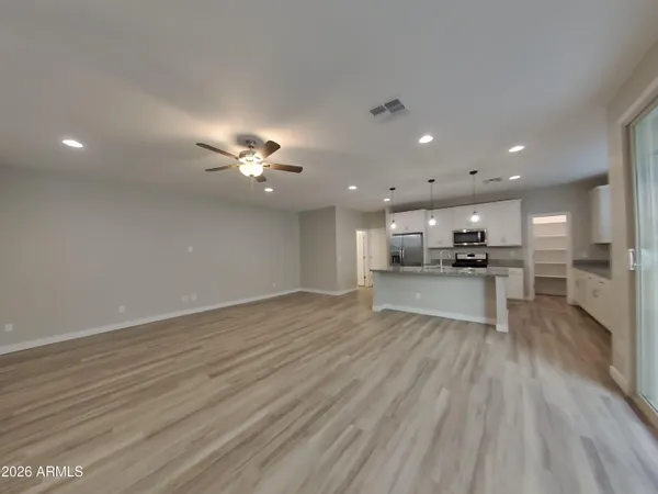 a view of an empty room and kitchen with wooden floor and fan