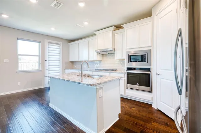 a kitchen with stainless steel appliances granite countertop a refrigerator a sink dishwasher a stove and white countertops with wooden floor