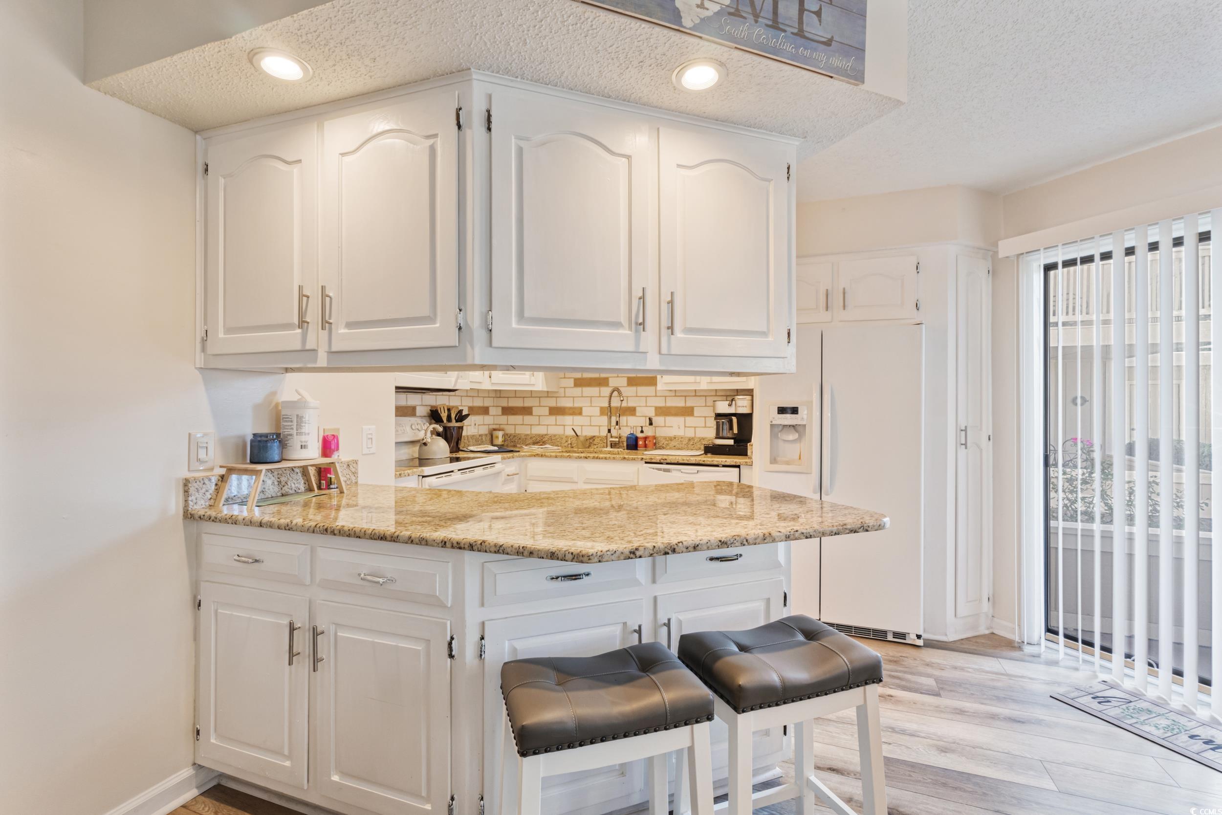 4242 Pinehurst Circle, Unit N3 Little River, SC 29566 - Photo 11 of 30 Kitchen featuring white cabinetry, white refrigerator with ice dispenser, a peninsula, tasteful backsplash, and a kitchen bar