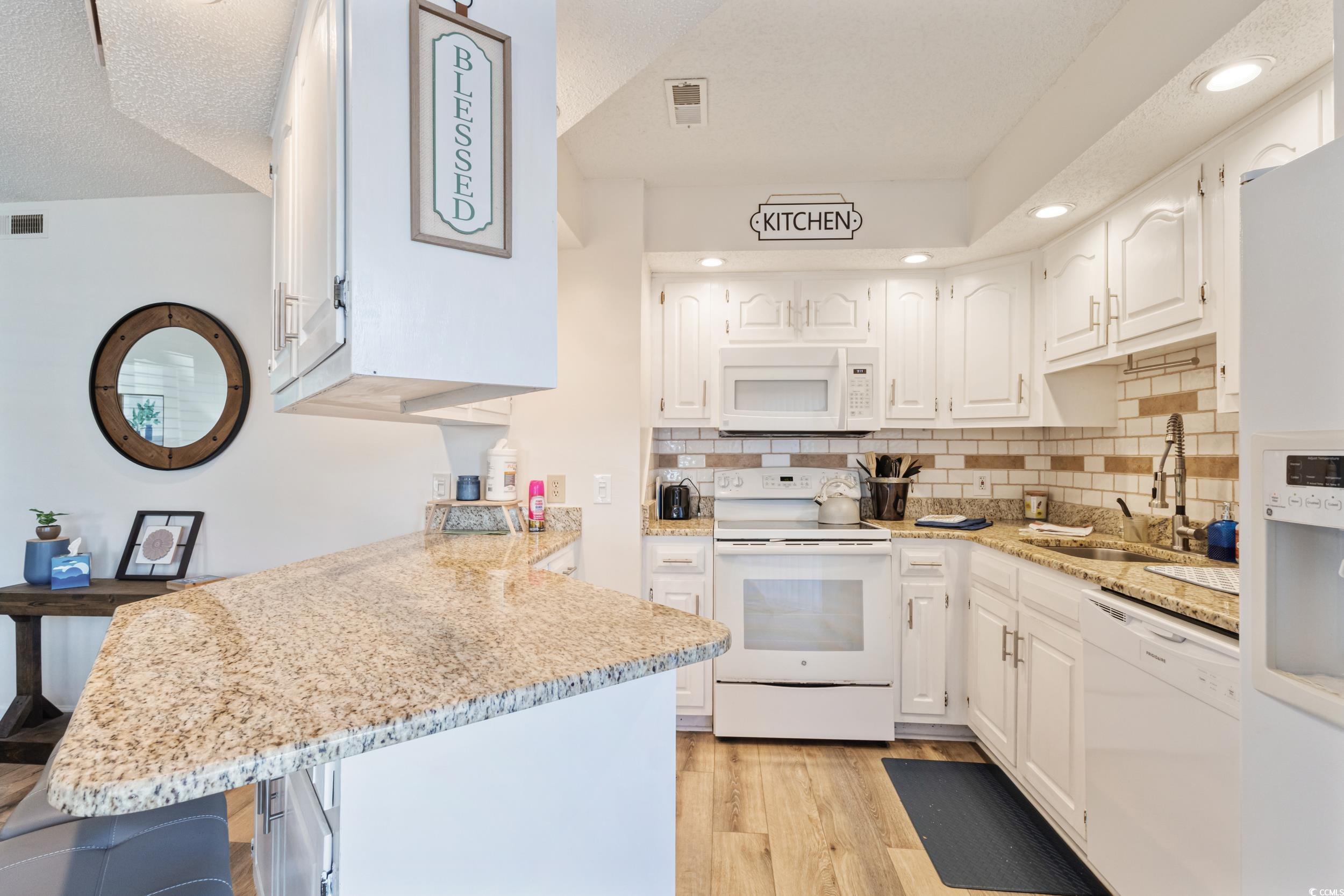 4242 Pinehurst Circle, Unit N3 Little River, SC 29566 - Photo 12 of 30 Kitchen featuring white appliances, a peninsula, white cabinets, tasteful backsplash, and recessed lighting