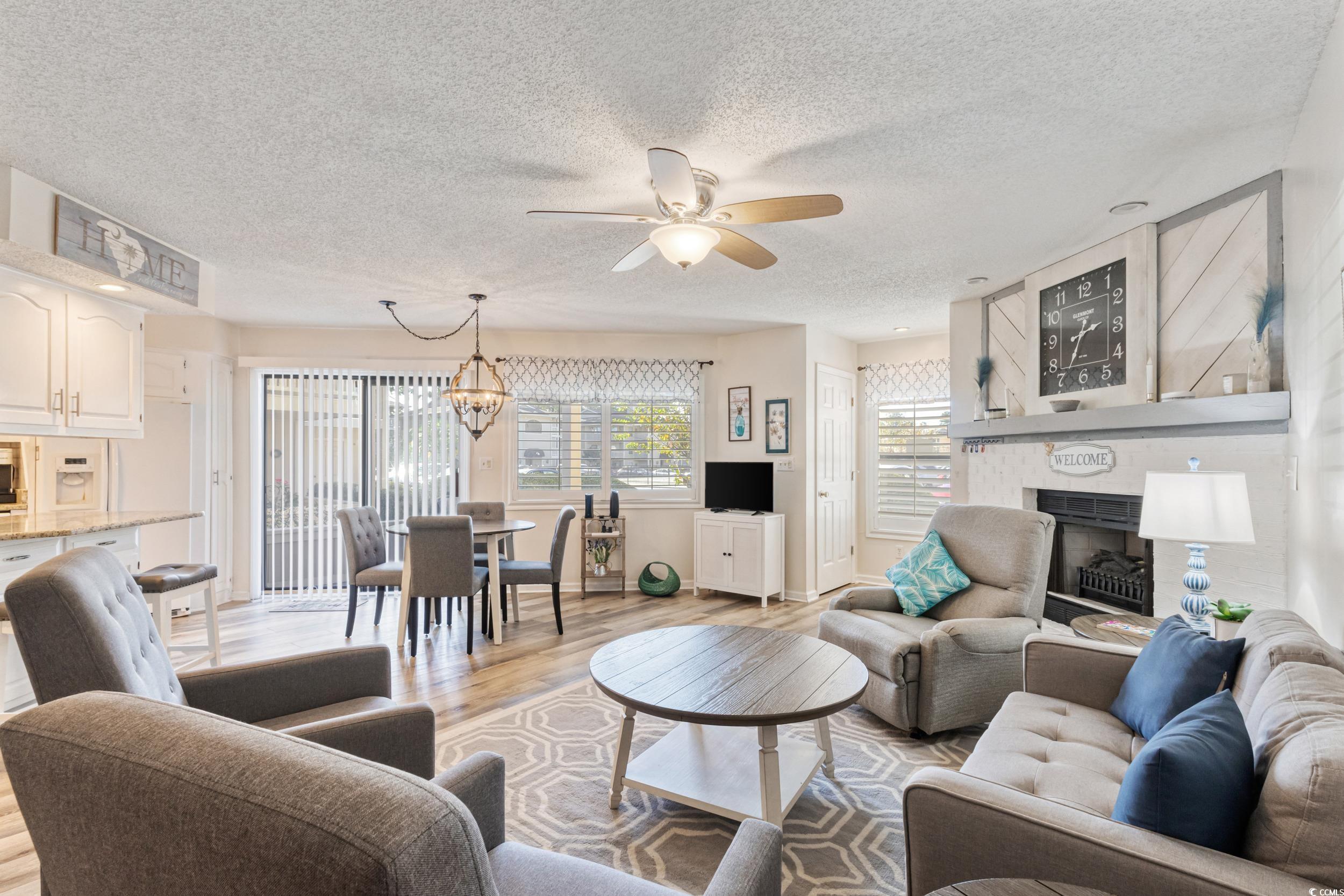 4242 Pinehurst Circle, Unit N3 Little River, SC 29566 - Photo 7 of 30 Living room with light wood finished floors, a fireplace, a chandelier, a textured ceiling, and ceiling fan