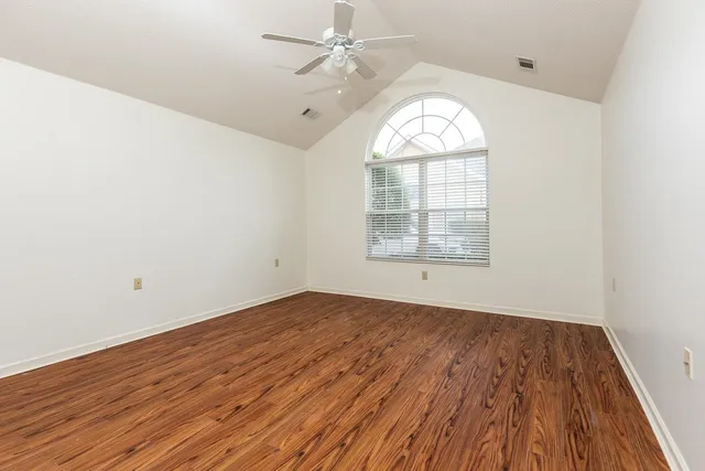 an empty room with wooden floor chandelier fan and windows