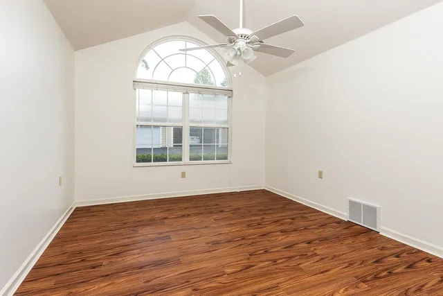 an empty room with wooden floor fan and windows