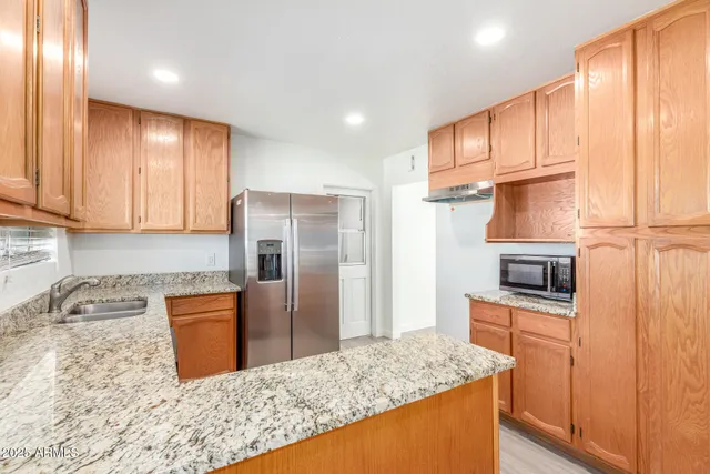 a kitchen with stainless steel appliances granite countertop a refrigerator a stove and a sink with wooden floor