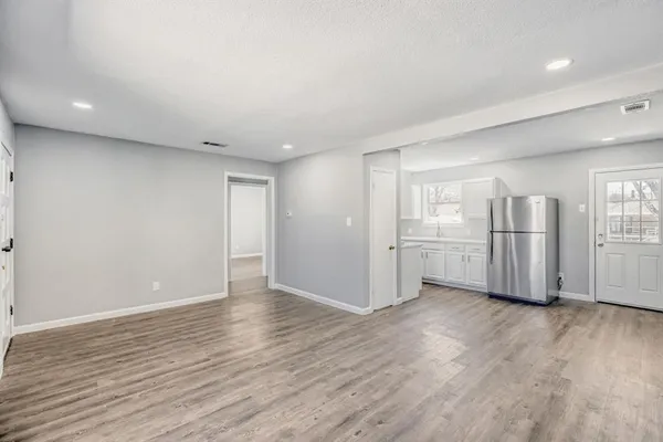 a view of an empty room with wooden floor and kitchen space