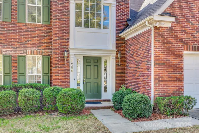 a view of a brick house with a yard plants and large tree